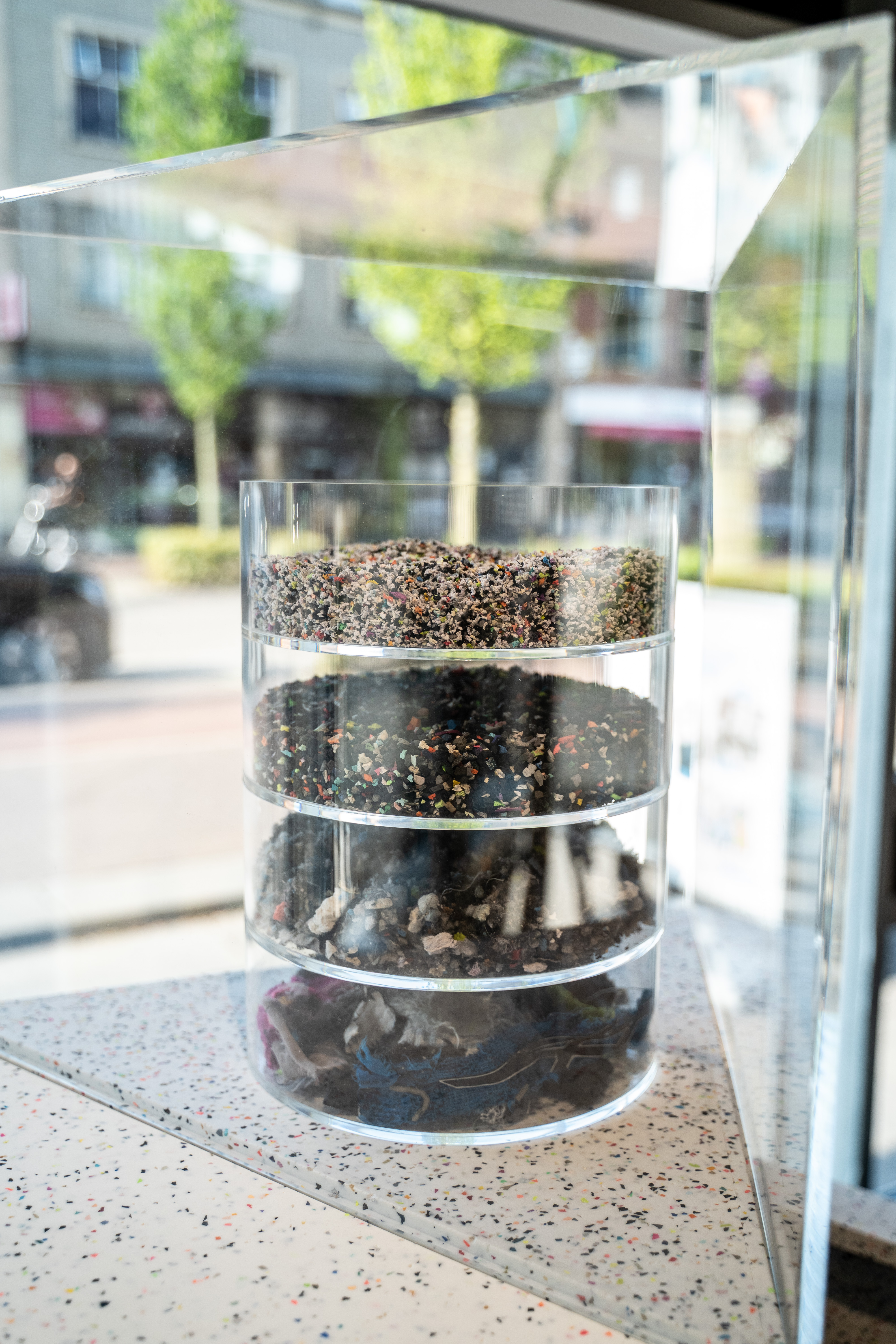 Separated material layers from recycled shoes displayed in a glass cylinder in-store